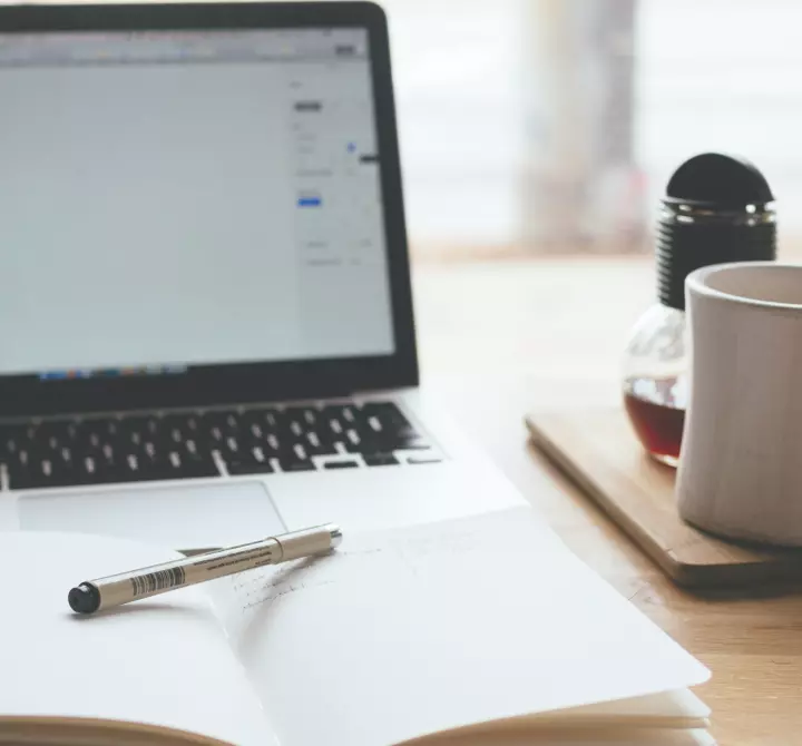 A notebook, pen and laptop on a work table.